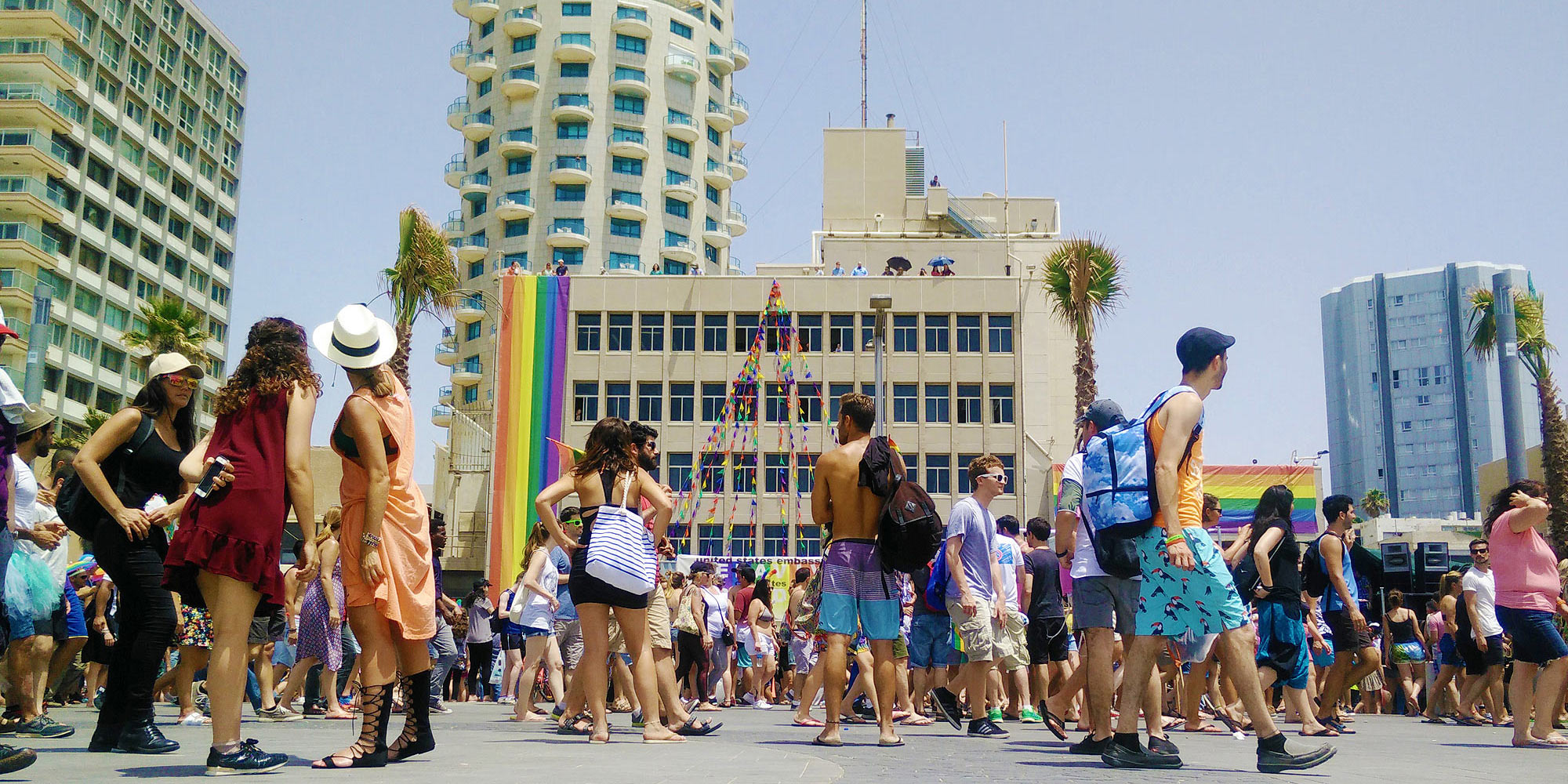 Teilnehmer des Tel Aviv Prides gehen die Strandpromenade vor der US-Botschaft mit langer Regenbogen-Flagge und dem Hotel Isrotel vorbei